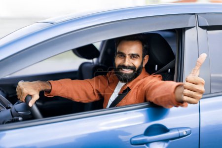 Foto de Me gusta conducir. Sonriendo tipo árabe sentado dentro del coche y mostrando el pulgar hacia arriba, aprobando su nuevo vehículo sonriendo a la cámara. Feliz conductor de Oriente Medio alquiler de automóviles para el viaje de fin de semana - Imagen libre de derechos