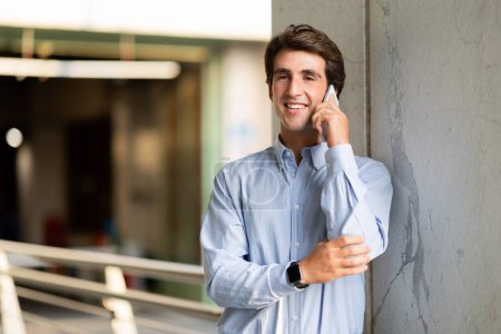Photo for Communication concept. Cheerful handsome young businessman standing outdoors with mobile phone. Employee professional talking on phone next to office building, looking at copy space and smiling - Royalty Free Image