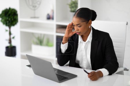 Téléchargez les photos : Femme d'affaires noire sérieuse travaillant sur ordinateur portable et résoudre des problèmes de tâches difficiles, assis sur le lieu de travail à l'intérieur, espace libre. Bureau routine de travail - en image libre de droit