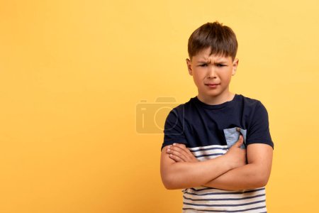 Foto de Enojado ofendido niño de edad escolar infeliz con camiseta casual con las manos cruzadas en el pecho mirando a la cámara con la cara furiosa resentido, aislado en el fondo amarillo, espacio de copia - Imagen libre de derechos