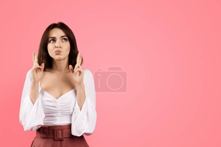 Photo for Positive pensive millennial caucasian brunette woman crossed her fingers and dreaming, isolated on pink background, studio. Good news, ad and offer, wish, hope and lifestyle - Royalty Free Image