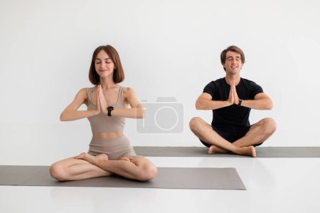 Glad young caucasian lady and guy in sportswear enjoy workout together, meditate, practice yoga in gym or room interior. Health care at home, lifestyle, sport, breathing exercises