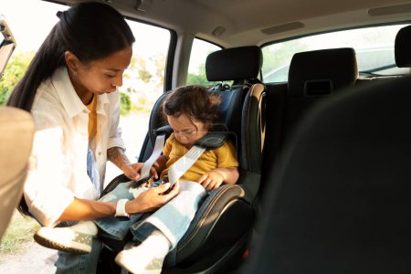 Photo for Auto Ride With Child. Korean Mom Sitting Down Her Baby Daughter In Safe Car Seat For Kid, Adjusting Harness Straps For Safety, Preparing For Automobile Trip With Toddler, Going To Nursery School - Royalty Free Image