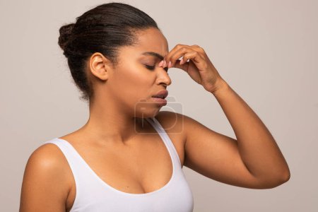 Foto de Mujer negra infeliz cansada con los ojos cerrados tocando el puente nasal, tiene migraña, que sufre de fiebre, gripe, resfriado, coronavirus, aislado sobre fondo gris, espacio de copia - Imagen libre de derechos