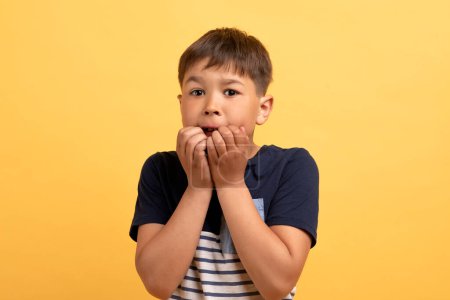 Photo for Frightened preteen boy wearing casual t-shirt biting his fists, emotional school aged child looking scared isolated on yellow background. Kids emotions concept, closeup studio shot - Royalty Free Image