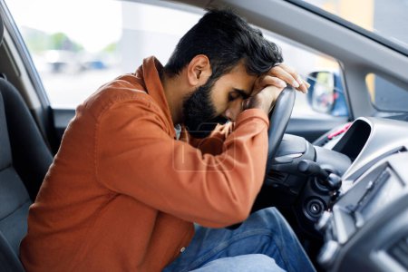 Foto de Unhappy Middle Eastern Driver Man Descansando la cabeza sobre la rueda sentado en el coche, durmiendo agotado durante el viaje. Un tipo desesperado teniendo problemas con su automóvil. Choque de vehículos, problema de propiedad del transporte - Imagen libre de derechos