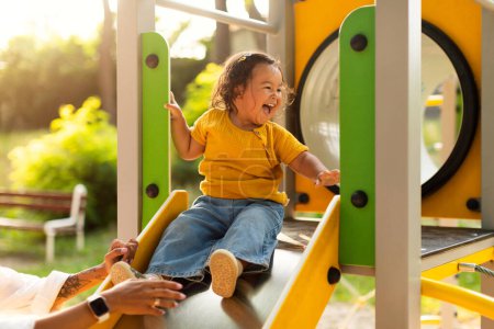 Photo for Adorable Chinese Baby Girl Riding Slides At Public Playground In Park, Mommy Catching Her Little Daughter, Having Fun And Playing Together. Toddler Child Enjoying Time At Play Ground With Mom - Royalty Free Image