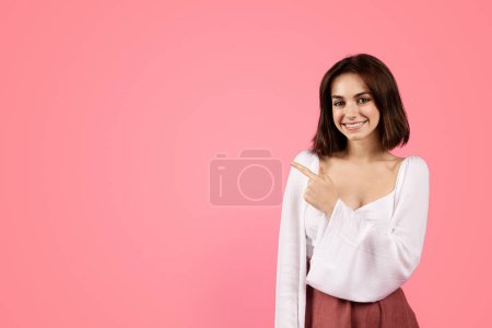 Photo for Cheerful millennial caucasian brunette woman pointing finger at empty space, isolated on pink background, studio. Beauty care recommendation, ad and offer, lifestyle and sale - Royalty Free Image