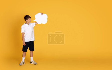 Téléchargez les photos : Choqué souriant adolescent caucasien montrant nuage abstrait pour la publicité et offre avec espace de copie, isolé sur fond de studio orange. Recommandation pour l'étude, l'éducation scolaire - en image libre de droit
