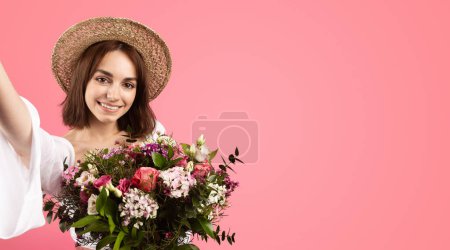 Téléchargez les photos : Souriante femme caucasienne millénaire en chapeau prendre selfie, profiter bouquet de fleurs, isolé sur fond rose, studio. Fête des fêtes, anniversaire, photo pour les réseaux sociaux, appel vidéo, blog - en image libre de droit