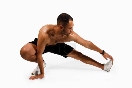Photo for Stretching fitness training. Sporty black guy exercising doing hamstring stretches, posing with shirtless torso on white background, studio shot. Sportsman stretching leg muscles before workout - Royalty Free Image