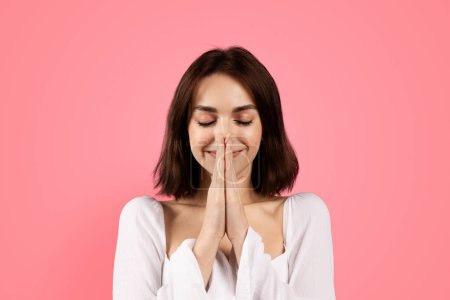 Photo for Happy pensive millennial caucasian brunette woman praying with hands, isolated on pink background, studio, close up. Make a wish, ad and offer, request and faith, hope and lifestyle - Royalty Free Image