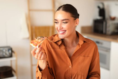 Photo for Happy young caucasian woman enjoy eating tasty homemade pizza, holding looking at slice and smiling, sitting in kitchen interior, free space - Royalty Free Image