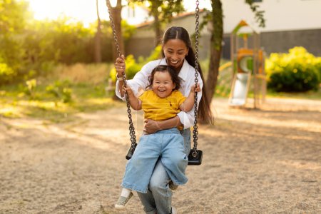 Photo for Korean Mommy Riding Little Baby Daughter Pushing Swings At Public Playground Outdoor, Mother And Her Kid Enjoying Entertainment And Activities Having Fun In City Park On Weekend - Royalty Free Image
