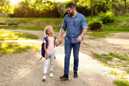 Photo for Parent and primary school pupil. Father accompanies the child girl to school, holding hand of his daughter, going to school or home after classes, full length, free space - Royalty Free Image