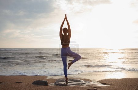 Photo for Millennial caucasian slim lady practice yoga, enjoy workout alone at sea beach, back, sun flare. Morning workout, sports, health care in morning, asana and lifestyle, motivation - Royalty Free Image