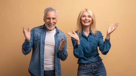 Téléchargez les photos : Incroyable excité heureux beau vieillard homme et femme en tenue denim décontractée gestuelle et souriante sur fond studio beige, montrant des émotions positives, bonheur, excitation - en image libre de droit