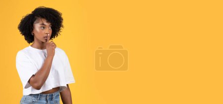 Photo for Serious young black curly lady in white t-shirt making shh gesture with hand, isolated on orange background, studio. Secret sign, lifestyle, ad and offer, gossip, good news - Royalty Free Image