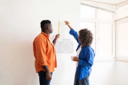 Photo for DIY Home Repair. Black Couple With Tape Ruler Measuring Wall In Room, Young African American Spouses Doing Renovation Of House, Taking Measurements Before Repairing, Woman Making Marks With Pencil - Royalty Free Image
