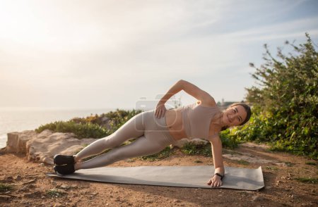 Photo for Cheerful slim millennial caucasian lady athlete in sportswear doing plank exercise on sea beach, enjoy sports alone outdoor. Fitness, body care and weight loss, active lifestyle - Royalty Free Image