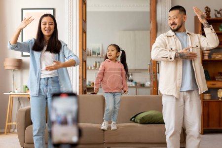 Photo for Family Content Creation. Korean influencers parents and little daughter dancing shooting video on smartphone, creating stream for blog and having fun together at home. Selective focus - Royalty Free Image