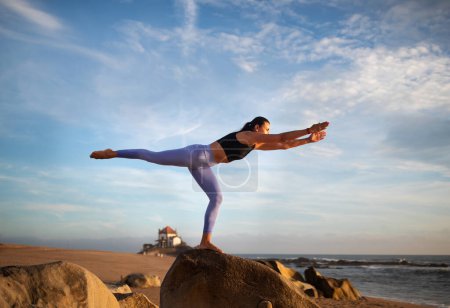 Téléchargez les photos : Millénaire dame caucasienne mince dans le yoga de pratique de vêtements de sport, profiter d'exercices de respiration, équilibre sur la plage de la mer. Entraînement seul, sport en plein air, soins de santé le matin, annonce, offre - en image libre de droit