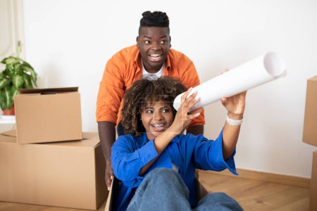 Photo for Positive African American Spouses Having Fun On Moving Day, Cheerful Man Pushing Cardboard Box With His Happy Wife, Excited Black Couple Fooling Together While Packing Things For Relocation, Closeup - Royalty Free Image