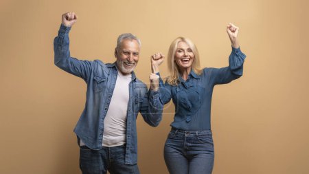 Téléchargez les photos : Émotionnel heureux heureux seniors hommes et femmes amis ou couple levant la main vers le haut et s'écriant sur fond beige. Conjoints de famille âgés joyeux célébrant le succès - en image libre de droit