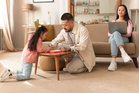 Photo for Famile Life and Work Balance. Korean Father Spending Time With Kid Daughter While Mother is Engaged in her Online Work With Laptop In Cozy Modern Living Room At Home. Selective Focus - Royalty Free Image