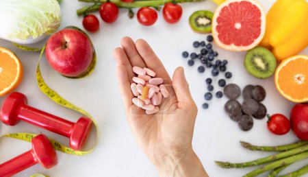 Hand of european adult lady recommends a lot of pills, vitamins, nutritional supplements on fruits, berries, vegetables, measuring tape and dumbbells background. Health care, diet, weight loss