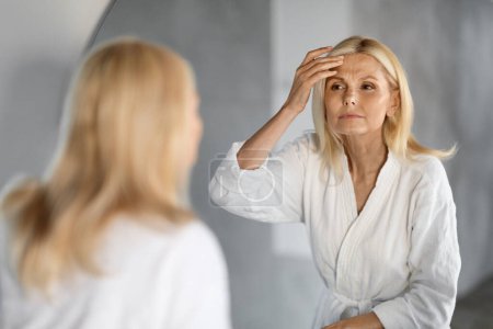 Photo for Mature Woman Looking In Mirror And Touching Wrinkles On Her Face, Upset Beautiful Senior Female Examining Fine Lines On Forehead, Suffering Skin Aging, Selective Focus On Reflection, Closeup - Royalty Free Image
