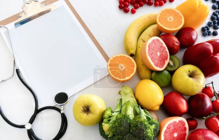 Photo for Stethoscope, paper on tablet with empty space, fruits, berries and vegetables, isolated on white studio background, top view. Health care, medical diet, weight loss, ad and offer - Royalty Free Image