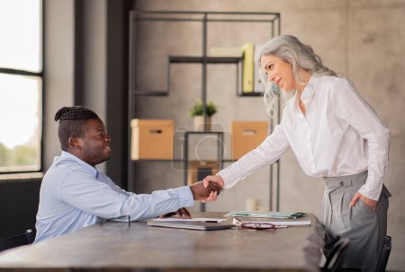 Hiring, Job Interview. Diverse Business Man And Woman Handshaking Meeting In Modern Office Interior. Applicant Shaking Hands With HR Manager Sitting At Table At Workplace. Side View Shot