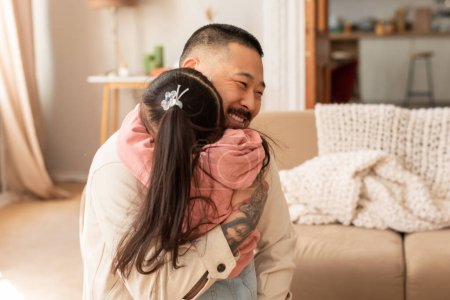Foto de Amor incondicional. Joyful Asian Dad abraza a su adorable hija en el interior de la sala. Niña y su padre expresando afecto y vínculo a través del abrazo en casa. Concepto de alegría de crianza - Imagen libre de derechos