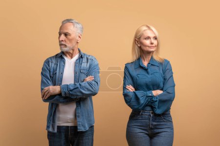 Photo for Problems in marriage, difficulties in relationships concept. Upset unhappy elderly married couple have quarrel, standing apart with arms crossed on chest, dont talk to each other, beige background - Royalty Free Image