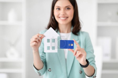 Photo for Glad young caucasian businesswoman in suit hold credit card and house in office interior. Real estate investment, business, realtor work, profit, professional recommendations loan - Royalty Free Image