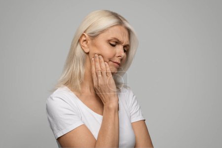 Photo for Closeup of sad mature woman touching her cheek, rubbing aching jawline, upset senior lady having tooth pain, suffering strong toothache, standing over grey studio background, copy space - Royalty Free Image