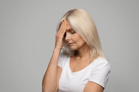 Photo for Headache Concept. Sad Mature Lady Suffering From Migraine Pain, Touching Her Forehed And Frowning, Senior Woman Feeling Unwell While Standing Over Grey Background In Studio, Copy Space - Royalty Free Image