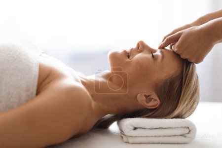 Photo for Peaceful middle aged woman getting healing head massage at modern luxury spa, cosmetologist making acupressure treatment to beautiful mature female, rubbing her forehead, side view shot - Royalty Free Image