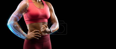 Foto de Estudio recortado de mujer afroamericana deportiva en ropa deportiva flexionando los músculos del brazo con hologramas futuristas en sus manos, fondo negro, panorama, espacio de copia, pancarta para el concepto de deporte digital - Imagen libre de derechos