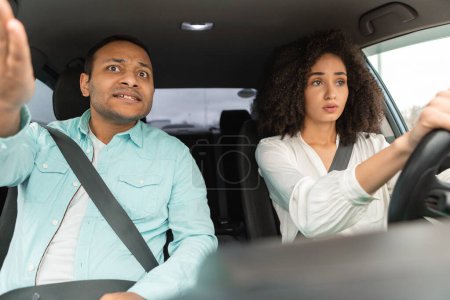 Téléchargez les photos : Arabe Femme Apprendre à conduire une voiture avec mécontent au volant enseignant pointant sur la route. Arabe homme éprouvant mécontentement tandis que sa femme au volant de leur nouvelle automobile, vue du tableau de bord - en image libre de droit