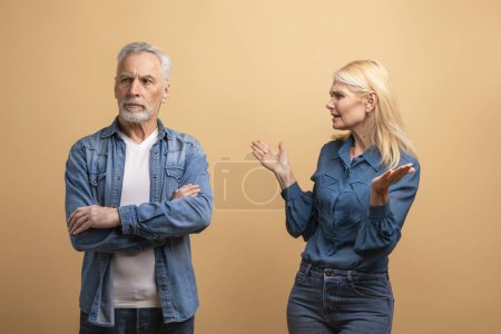 Photo for Unhappy marriage, crisis in relationships. Angry senior blonde woman wife scolding yelling at her frustrated offended husband grey-haired man, elderly couple fighting over beige studio background - Royalty Free Image