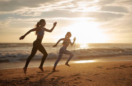Téléchargez les photos : Souriantes sœurs jumelles caucasiennes millénaires courir, profiter de l'entraînement à la plage de la mer. Entraînement cardio matinal, compétition, sport en plein air, soins de santé et mode de vie actif - en image libre de droit