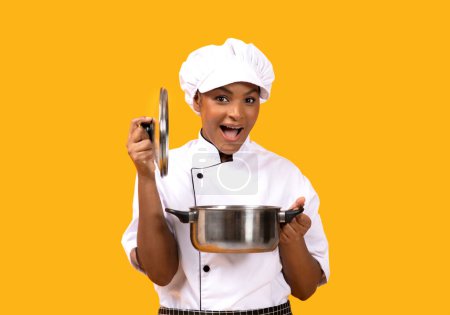 Photo for Surprised Young Black Chef Woman Opening Saucepan And Looking At Camera, Excited African American Cook Lady With Stewpot In Hands Posing Isolated Over Yellow Studio Background, Copy Space - Royalty Free Image