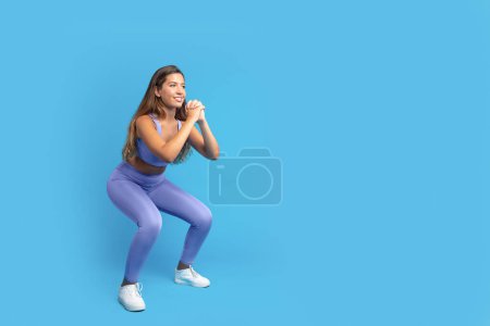Photo for Cheerful slim young caucasian lady in sportswear squat, enjoy cardio workout, isolated on blue studio background, full length. Fitness lifestyle, body care, weight loss, ad and offer - Royalty Free Image
