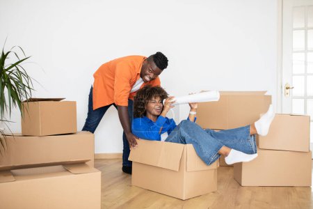 Photo for Cheerful Black Couple Having Fun Together While Relocating Home, Positive Young African American Spouses Fooling On Moving Day, Joyful Man Pushing Cardboard Box With His Happy Wife, Copy Space - Royalty Free Image
