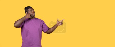 Photo for Dial this number. Positive black guy showing call me gesture and pointing finger aside at copy space, standing over yellow background in studio. Mobile communication. Panorama - Royalty Free Image