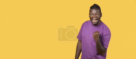 Photo for Emotional African American guy screaming in excitement, gesturing yes shaking clenched fist on yellow background. Joyful guy shouting celebrating success, cheering team. Panorama, copy space - Royalty Free Image
