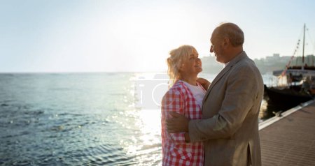 Téléchargez les photos : Conjoints aînés ayant des moments romantiques tout en marchant à l'extérieur sur la promenade près de la mer, Couple âgé heureux se détendre à l'extérieur, coller et regarder les uns les autres avec amour, Panorama avec espace de copie - en image libre de droit