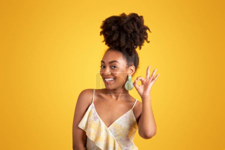 Photo for Glad millennial black lady in dress show ok sign with hand, isolated on orange background, studio. Sale, work, study recommendation, ad and offer, fashion and lifestyle, human emotions - Royalty Free Image